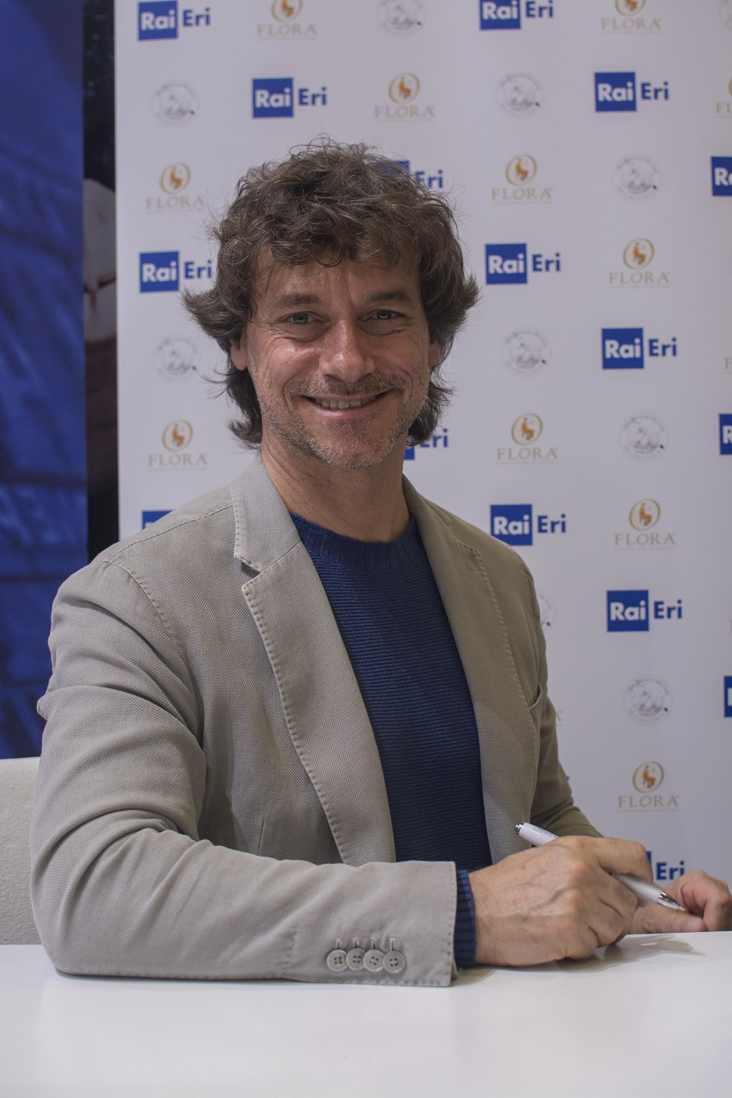 Alberto Angela sorride seduto a un tavolo durante una presentazione