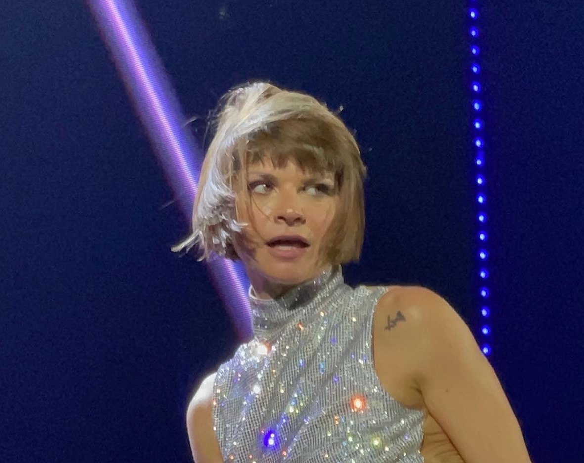 Alessandra Amoroso sul palco, capelli corti biondi e top argentato, guarda di lato