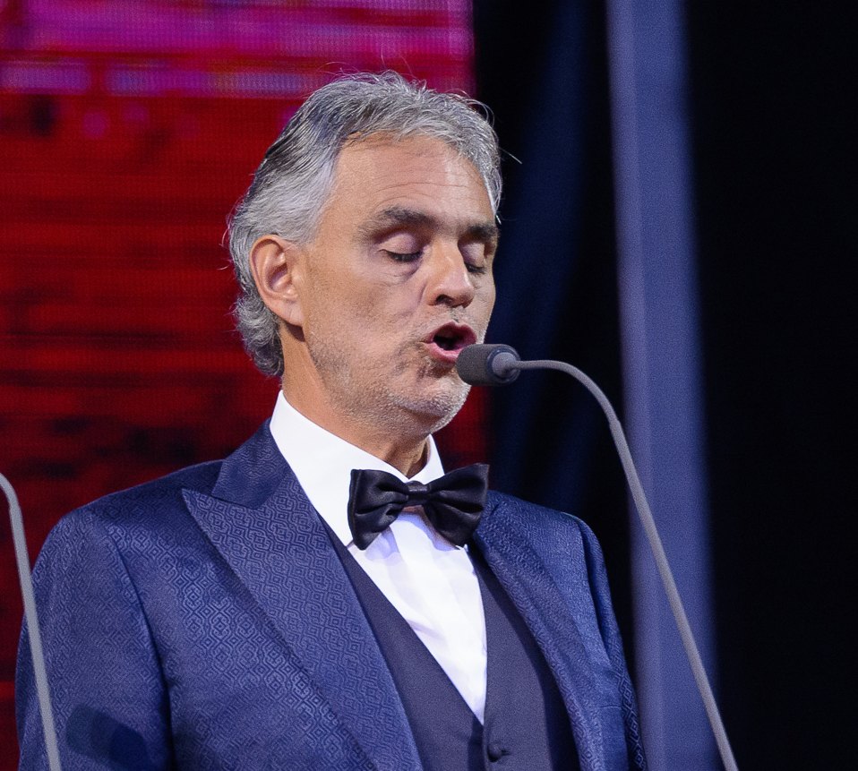 Andrea Bocelli canta al microfono sul palco, in smoking blu e papillon