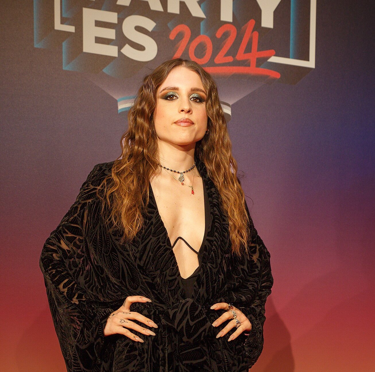 Angelina Mango posa con i capelli sciolti e un abito nero su un fondale colorato