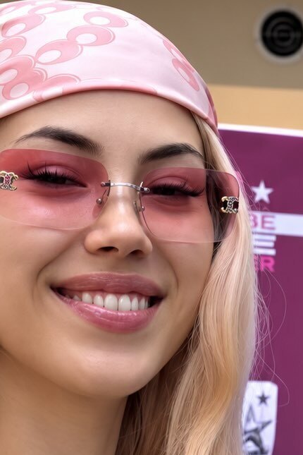 ANNA sorride in primo piano, bandana rosa e occhiali da sole rosa