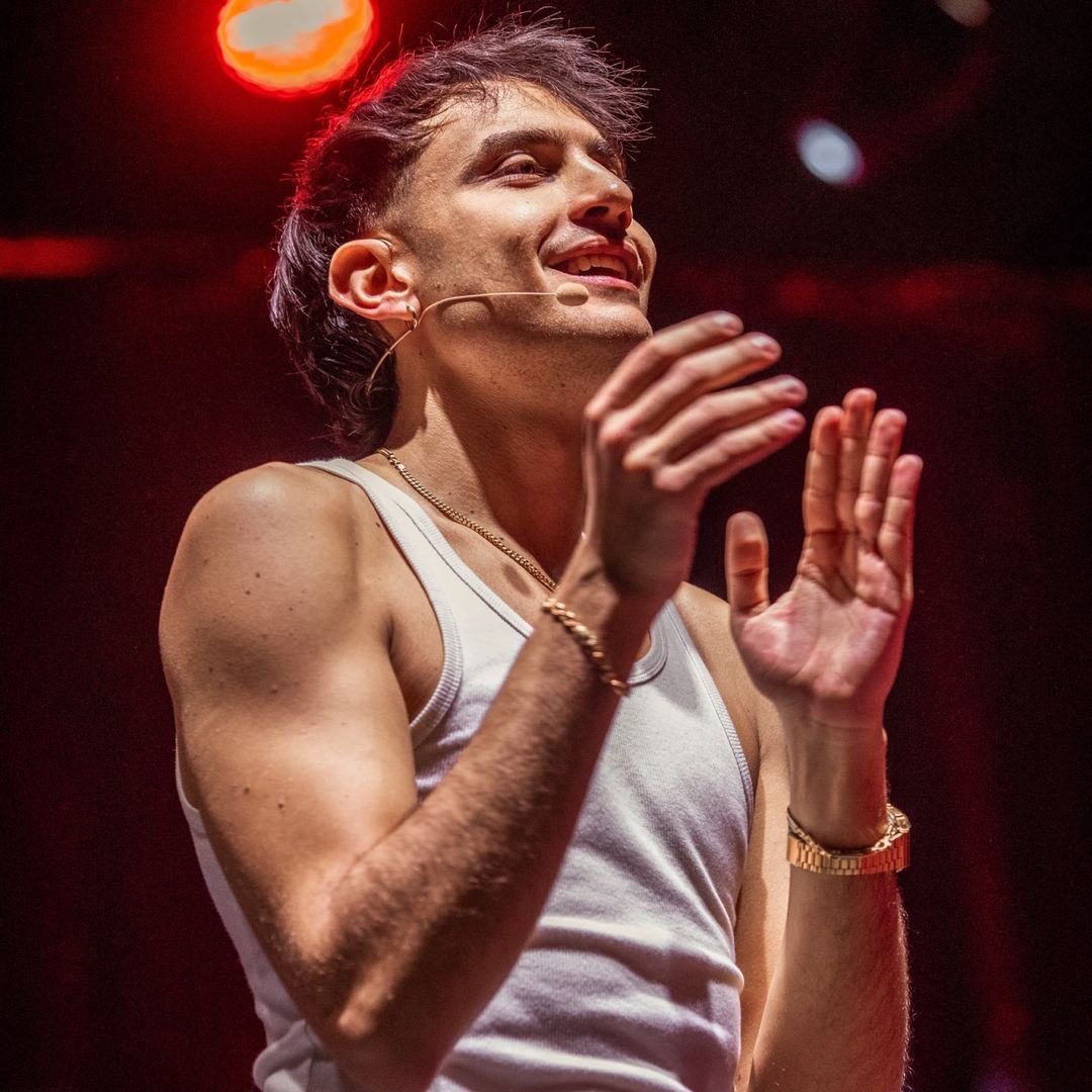 Awed sorride sul palco in canotta bianca, con il microfono ad archetto e le mani alzate