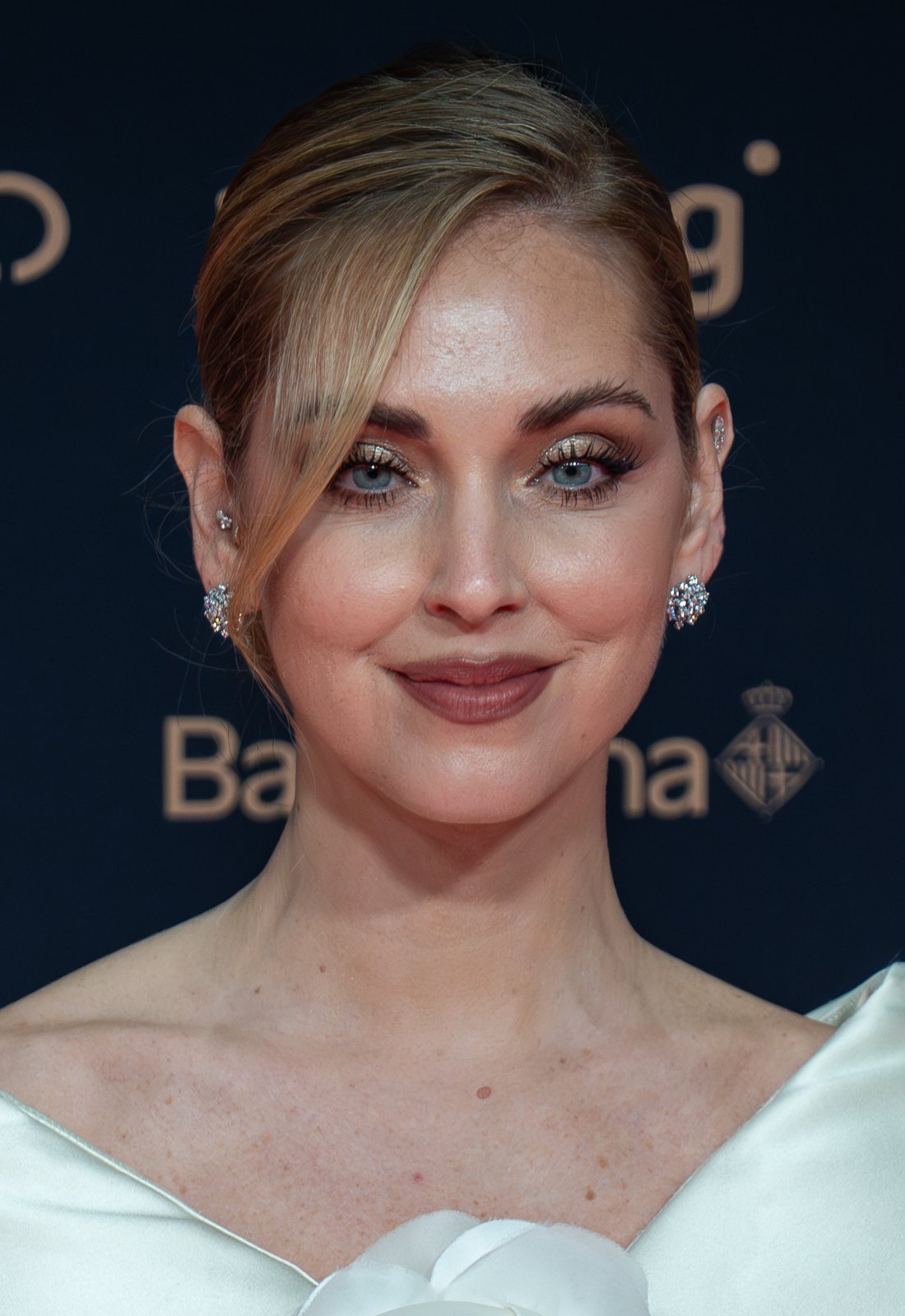 Chiara Ferragni sorride su un red carpet, capelli raccolti e orecchini di cristalli