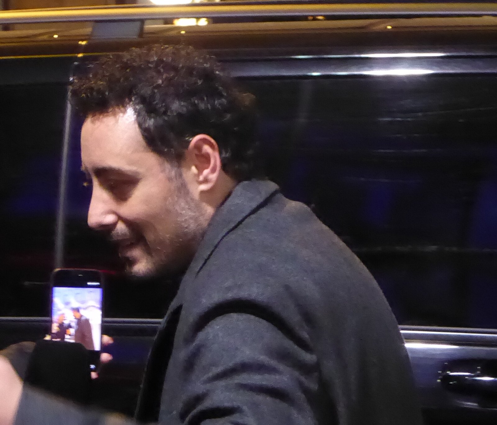 Ciro Priello sorride di profilo, di sera, mentre qualcuno lo riprende con il telefono