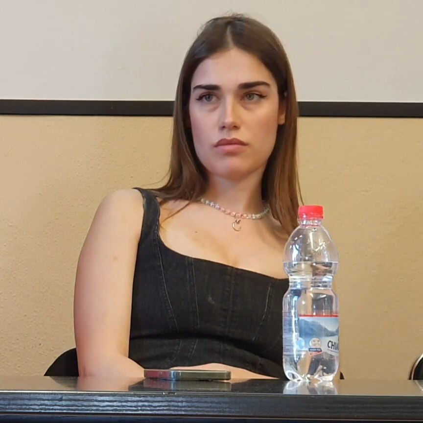 Clara seduta a un tavolo guarda davanti a sé durante un incontro