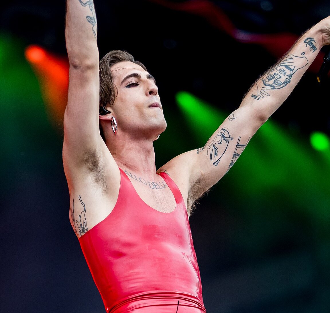 Damiano David dei Måneskin canta sul palco con le braccia alzate e una canotta rossa