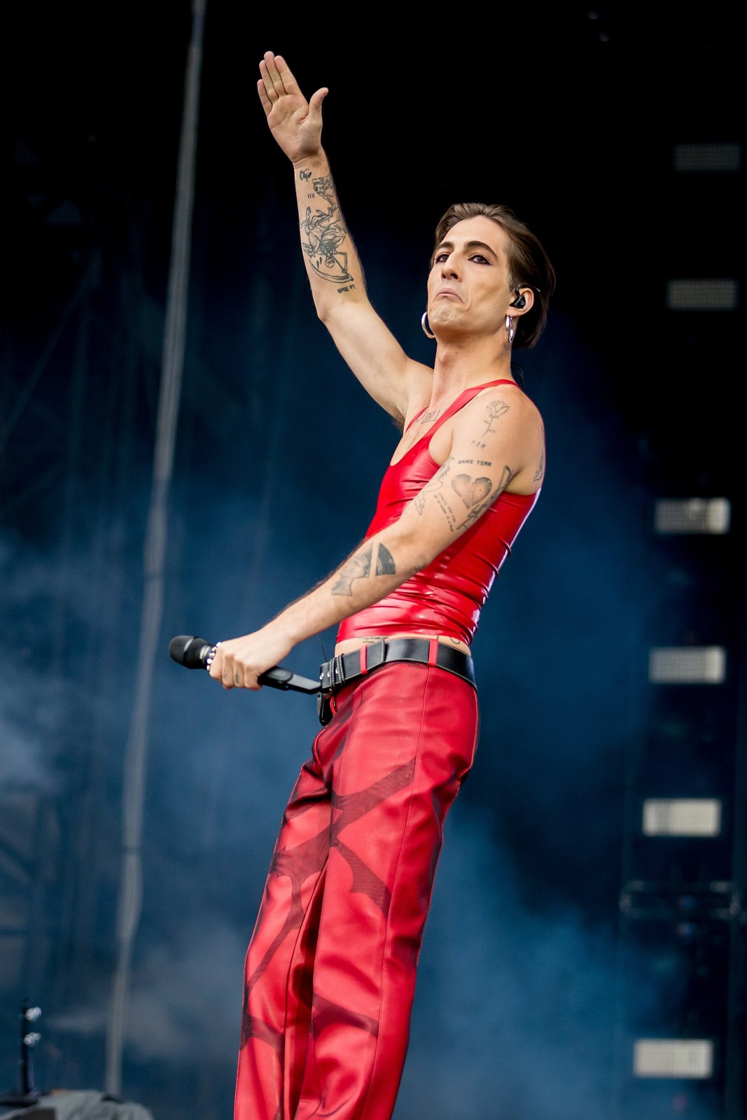 Damiano David canta sul palco con un braccio alzato e una canottiera rossa