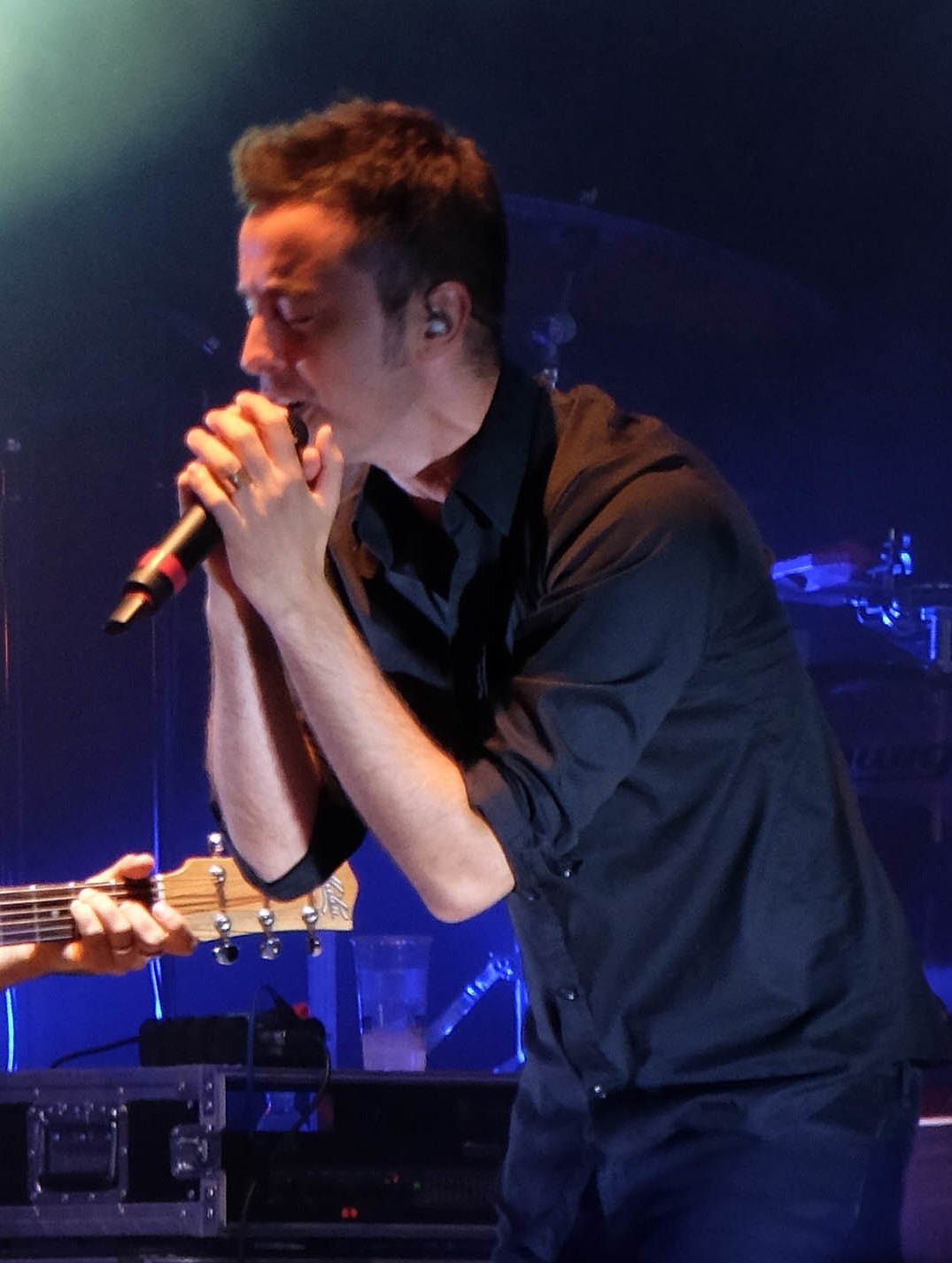 Diodato canta al microfono su un palco, luci blu alle spalle