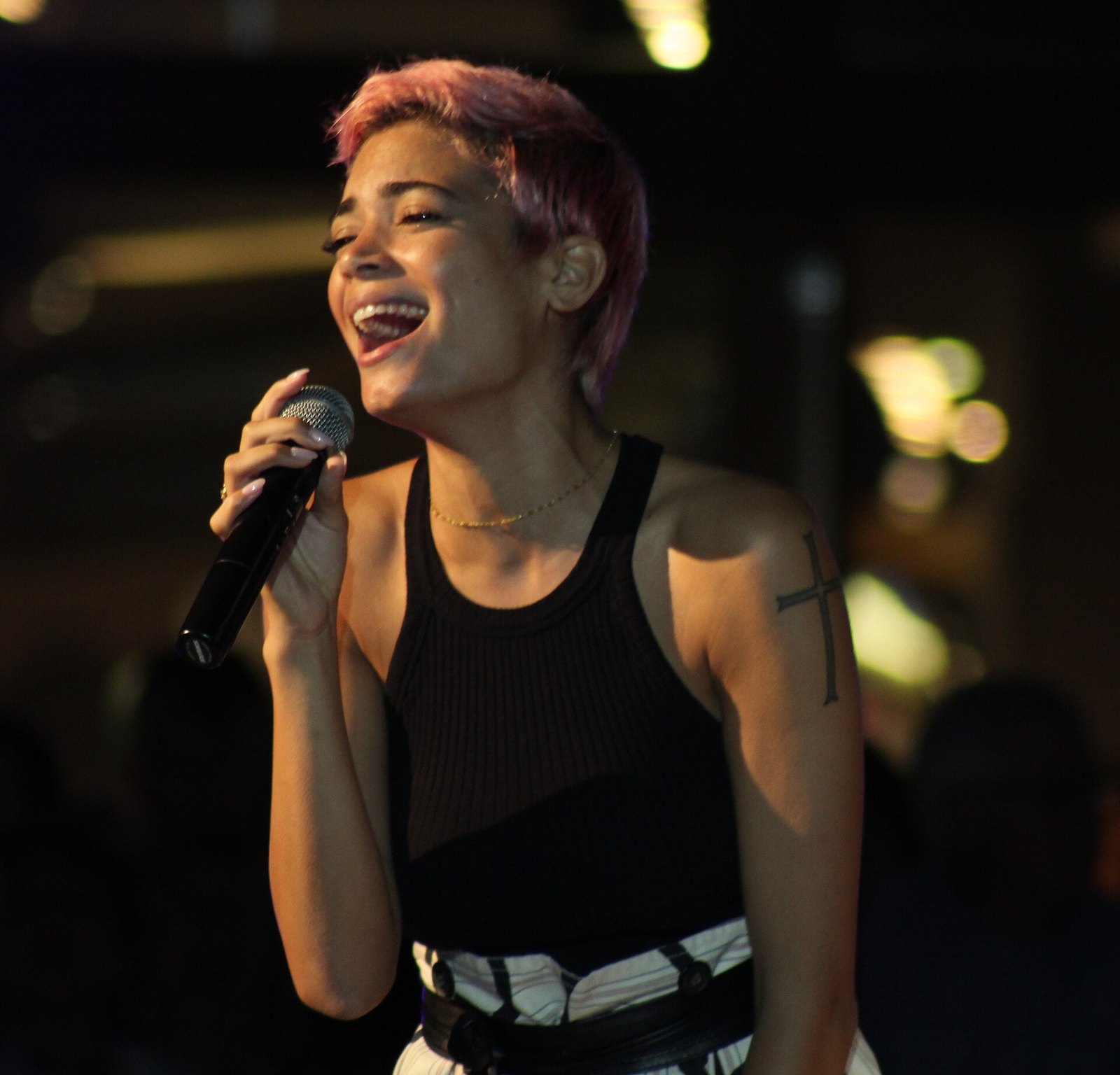 Elodie canta al microfono durante un concerto, con i capelli corti rosa