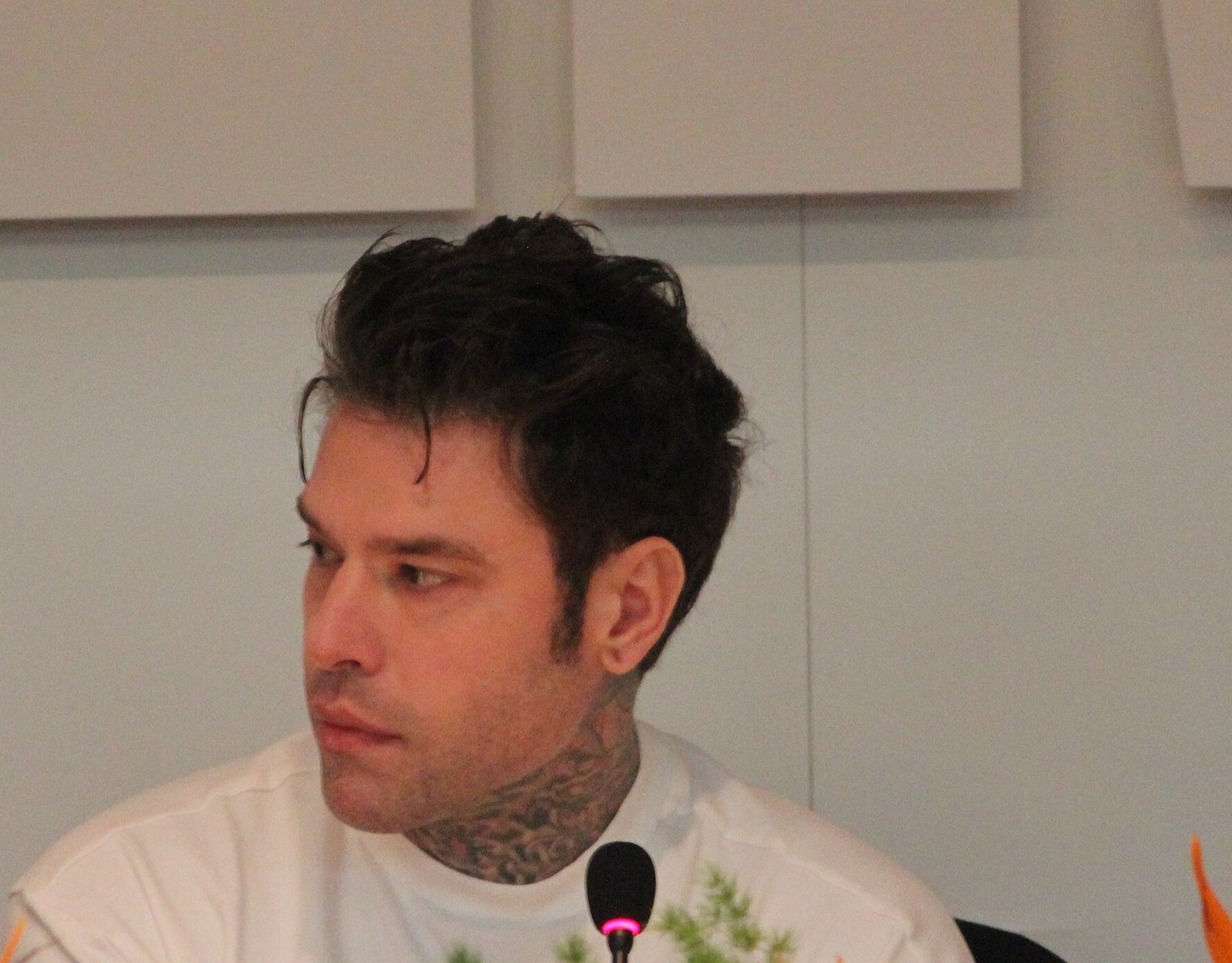 Fedez seduto in conferenza stampa a Sanremo 2026, maglietta bianca, guarda di lato