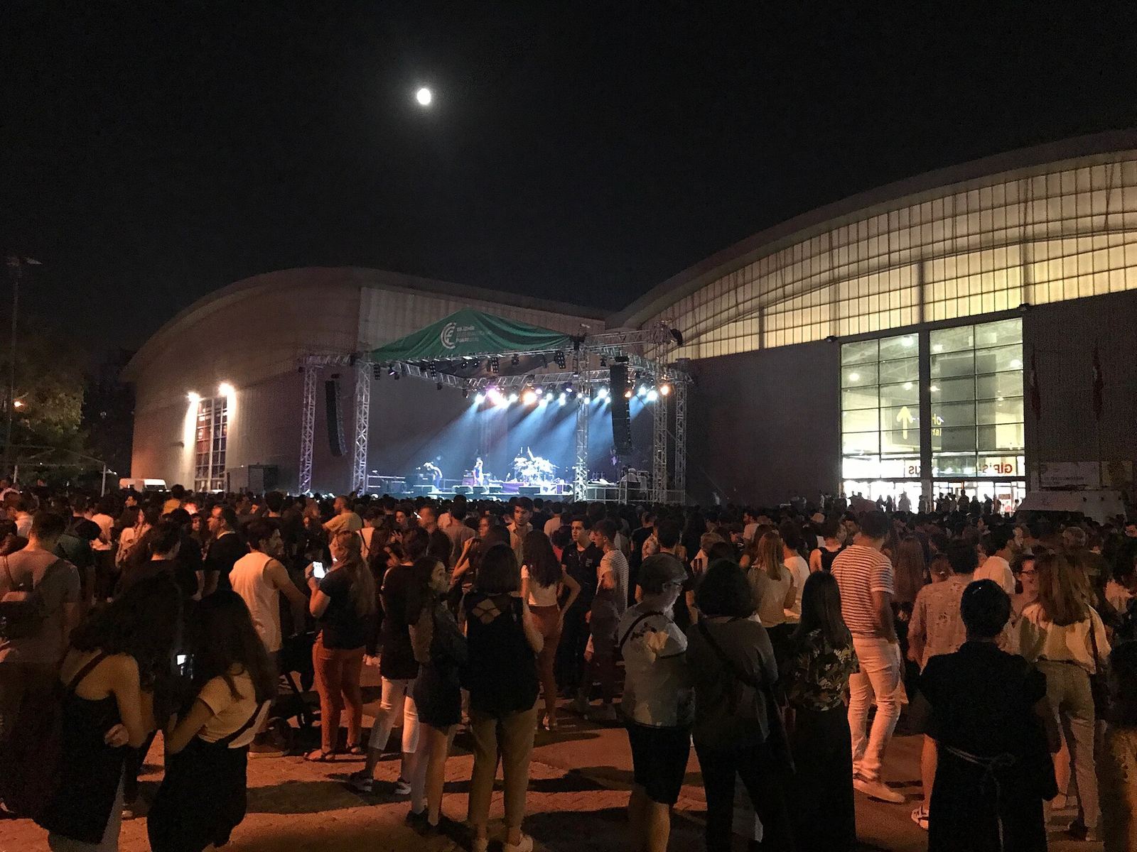 Pubblico in attesa davanti a un palco illuminato, di notte