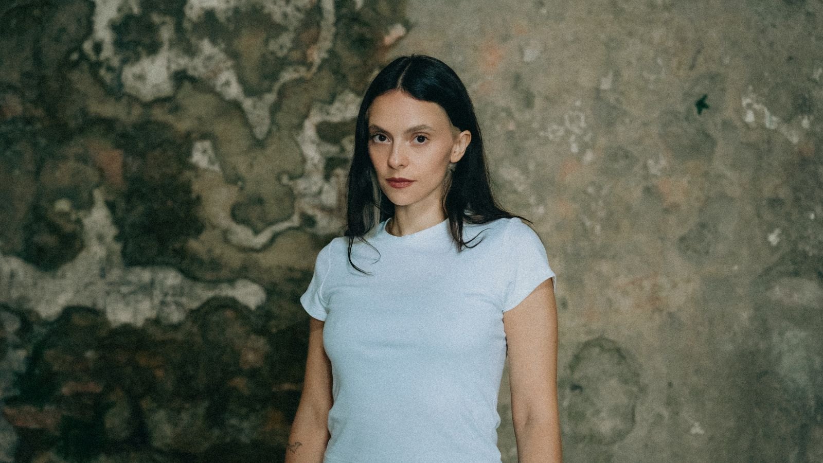 Francesca Michielin in maglietta azzurra davanti a un muro scrostato, guarda in camera