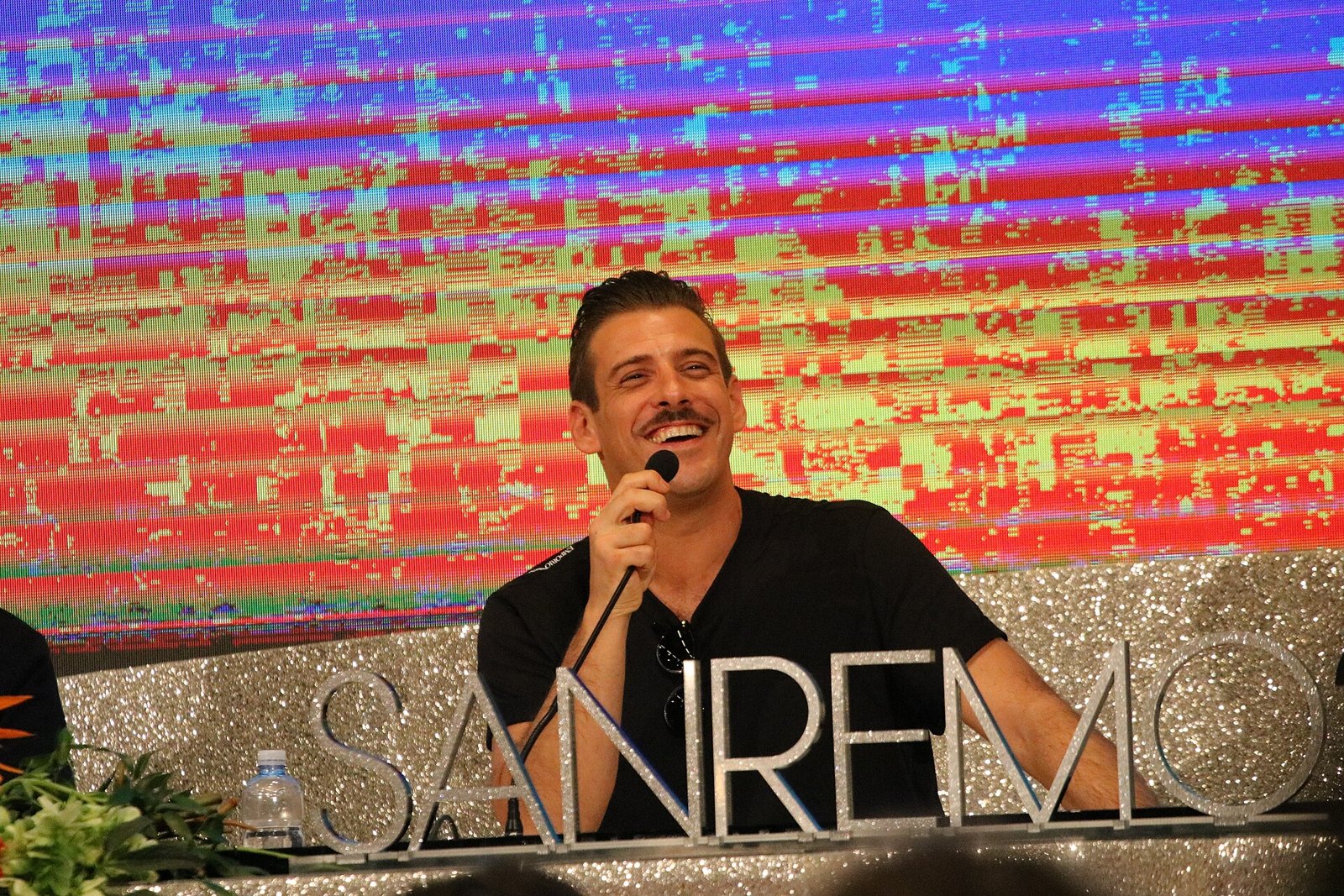 Francesco Gabbani sorride con il microfono in mano davanti a uno schermo colorato
