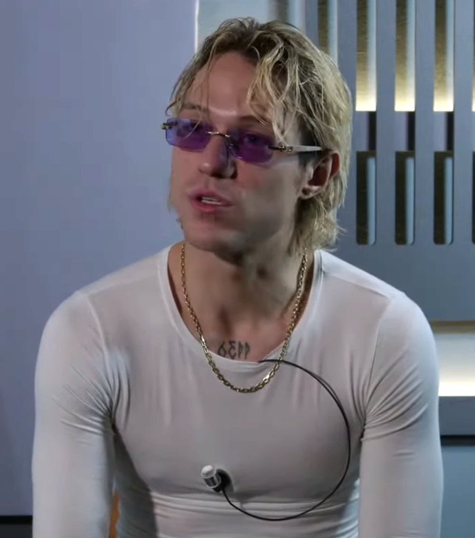 Irama con occhiali da sole viola e capelli biondi mossi, ripreso di tre quarti