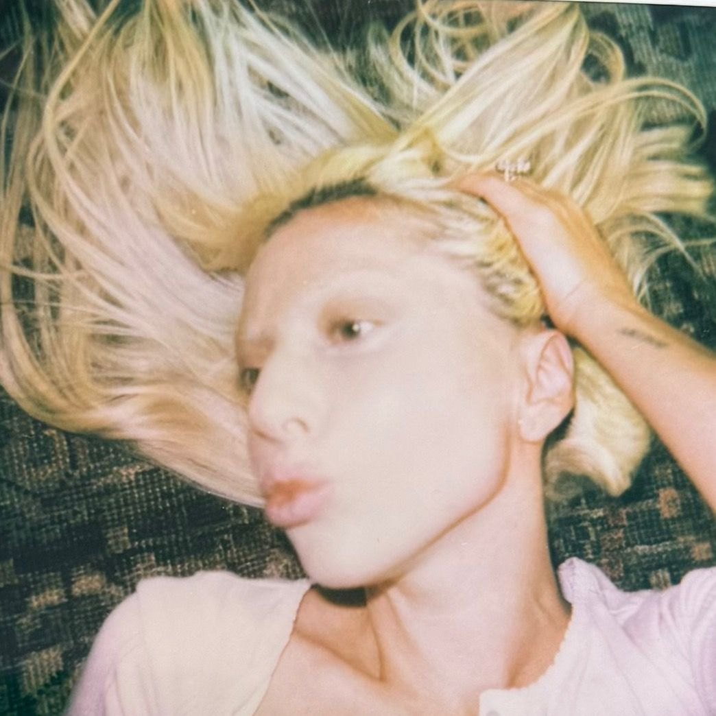 Lady Gaga sdraiata, primo piano del viso con i capelli biondi sparsi