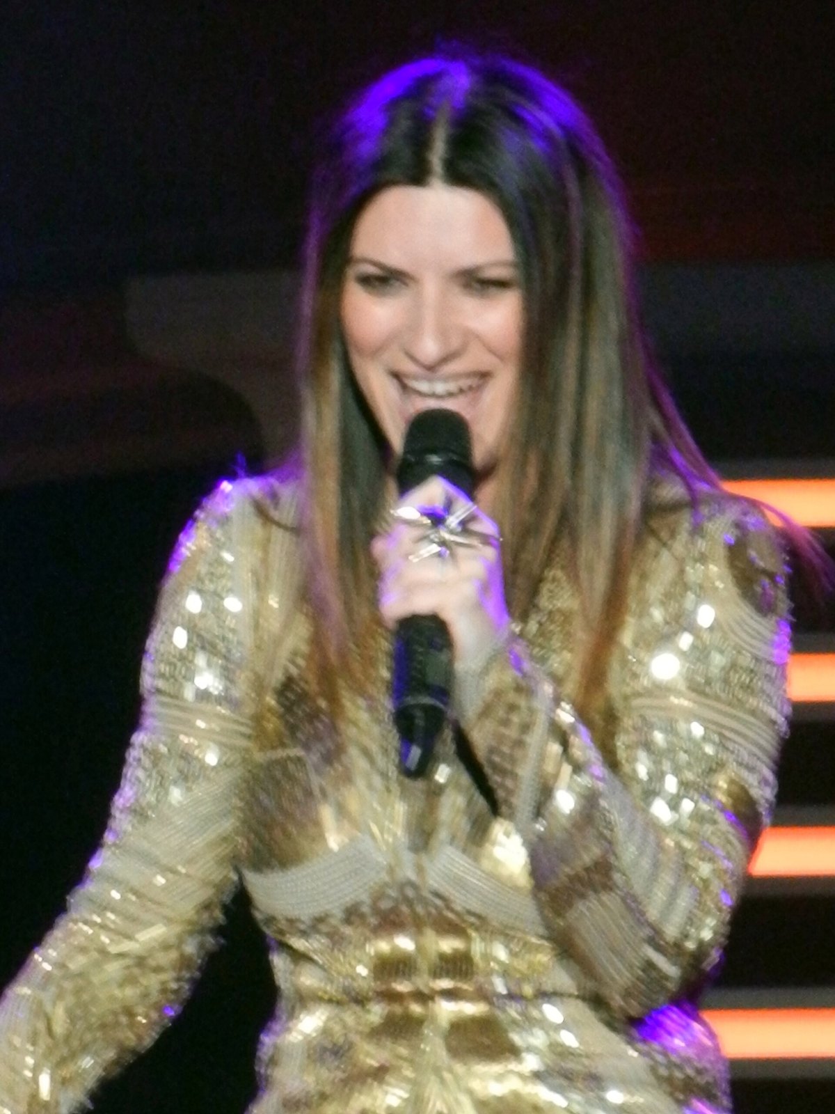 Laura Pausini sorride mentre canta al microfono sul palco