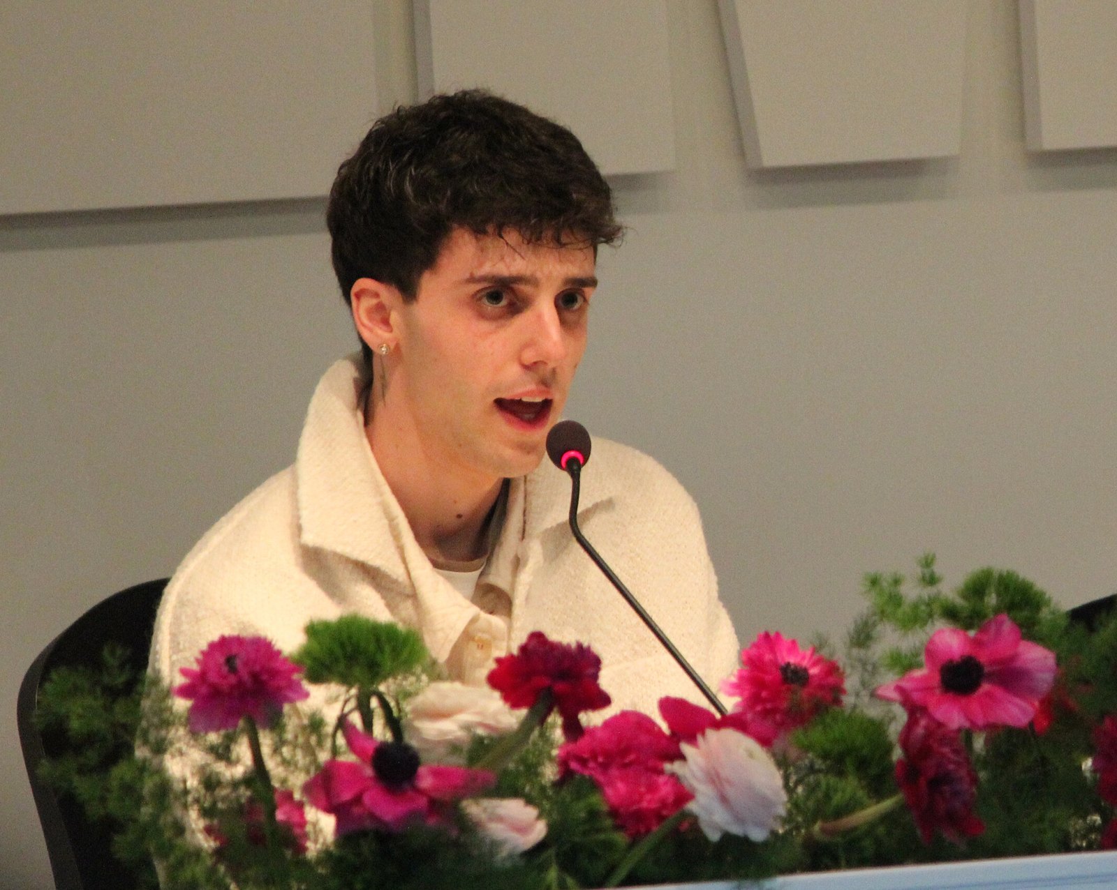 LDA parla al microfono durante una conferenza stampa, giacca bianca