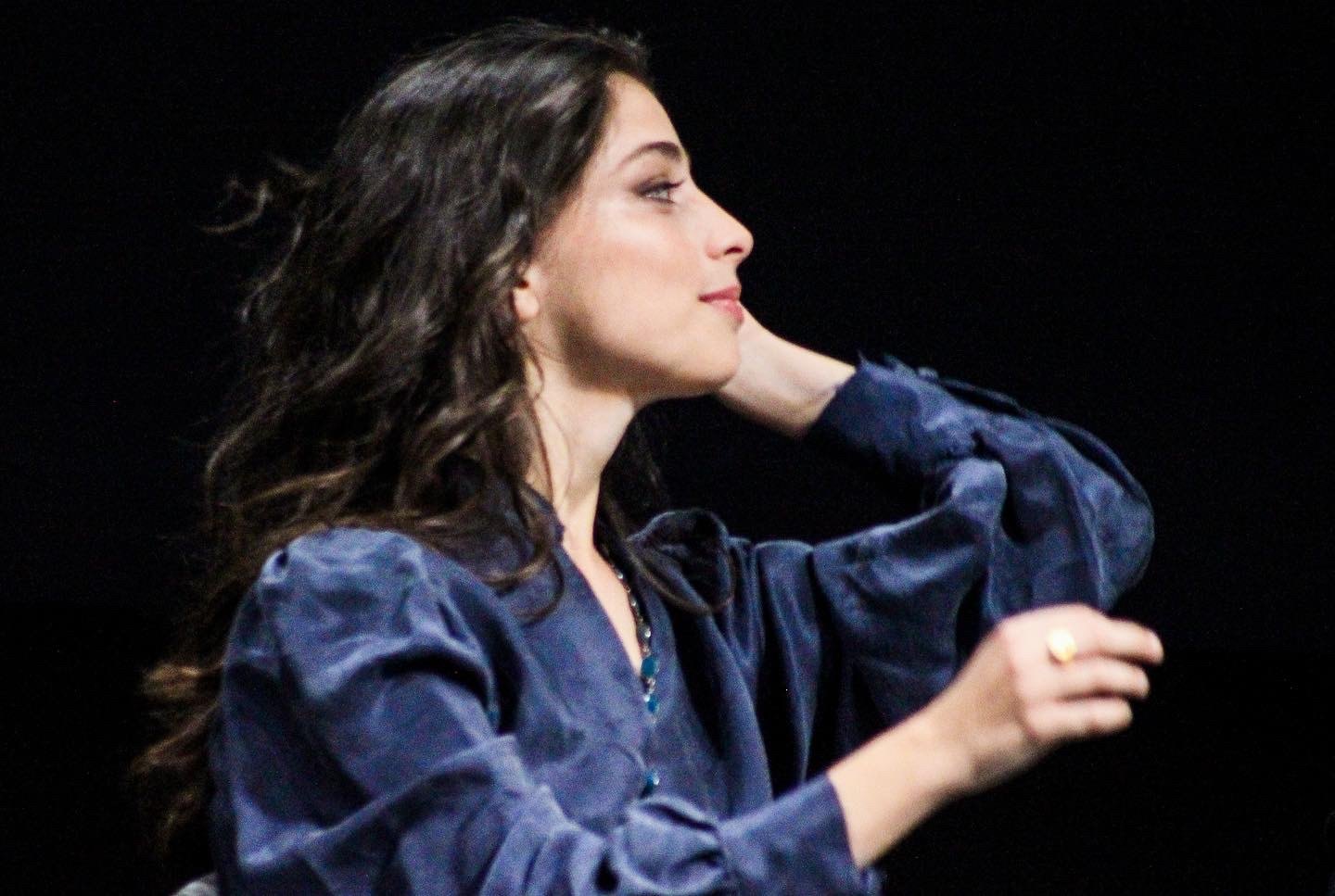 Lea Gavino di profilo durante un evento, con una camicia blu e i capelli mossi