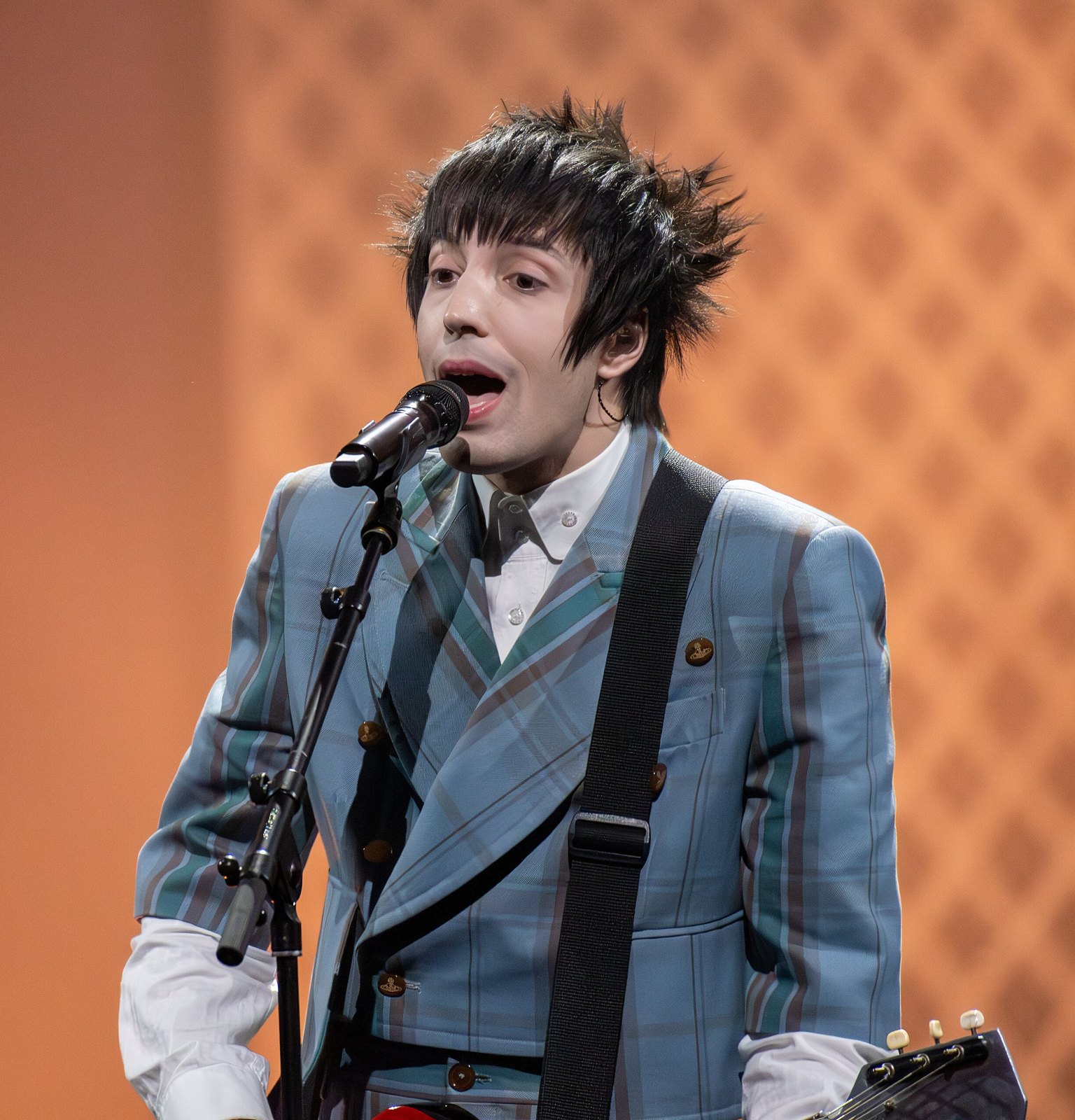 Lucio Corsi canta al microfono sul palco dell'Eurovision con la chitarra a tracolla