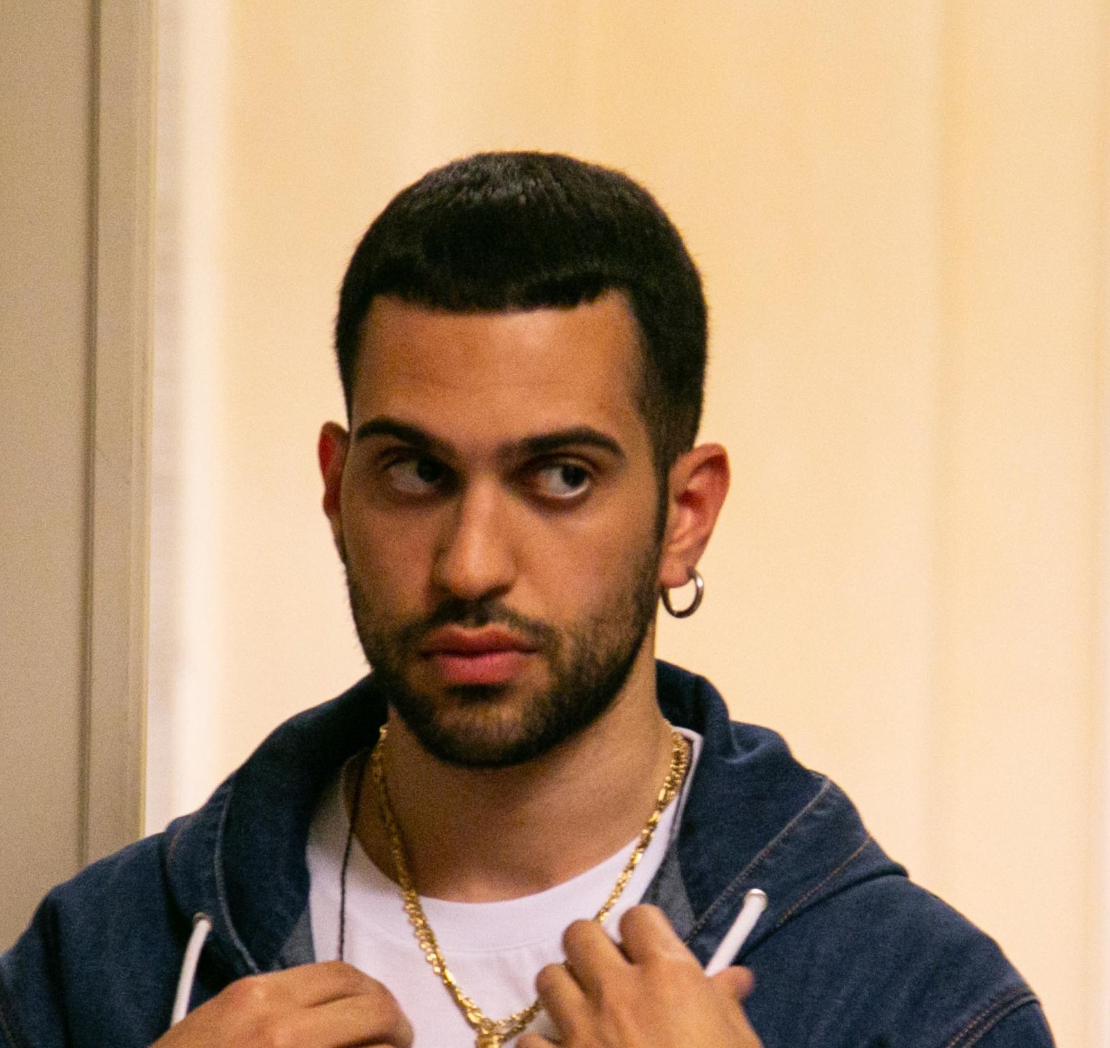 Mahmood in felpa di jeans e catena d'oro, guarda di lato