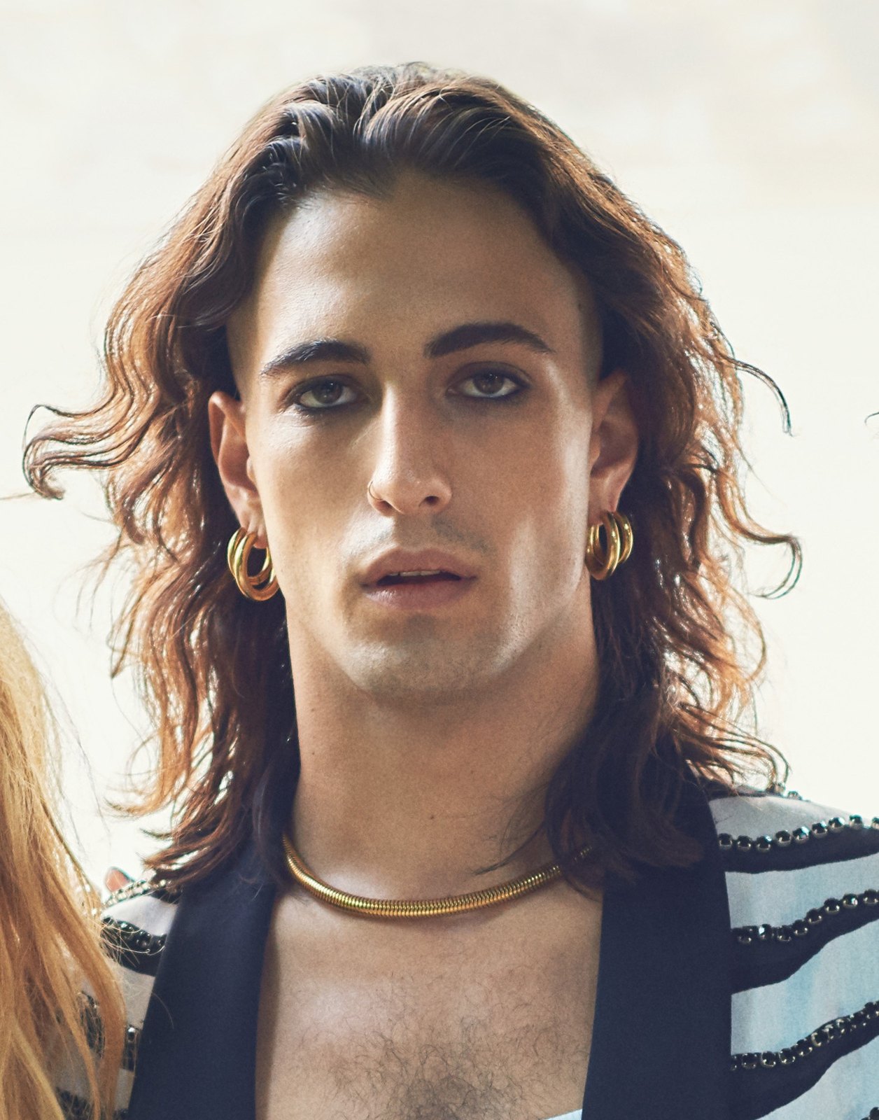 Damiano David dei Måneskin guarda in camera, capelli lunghi e orecchini dorati