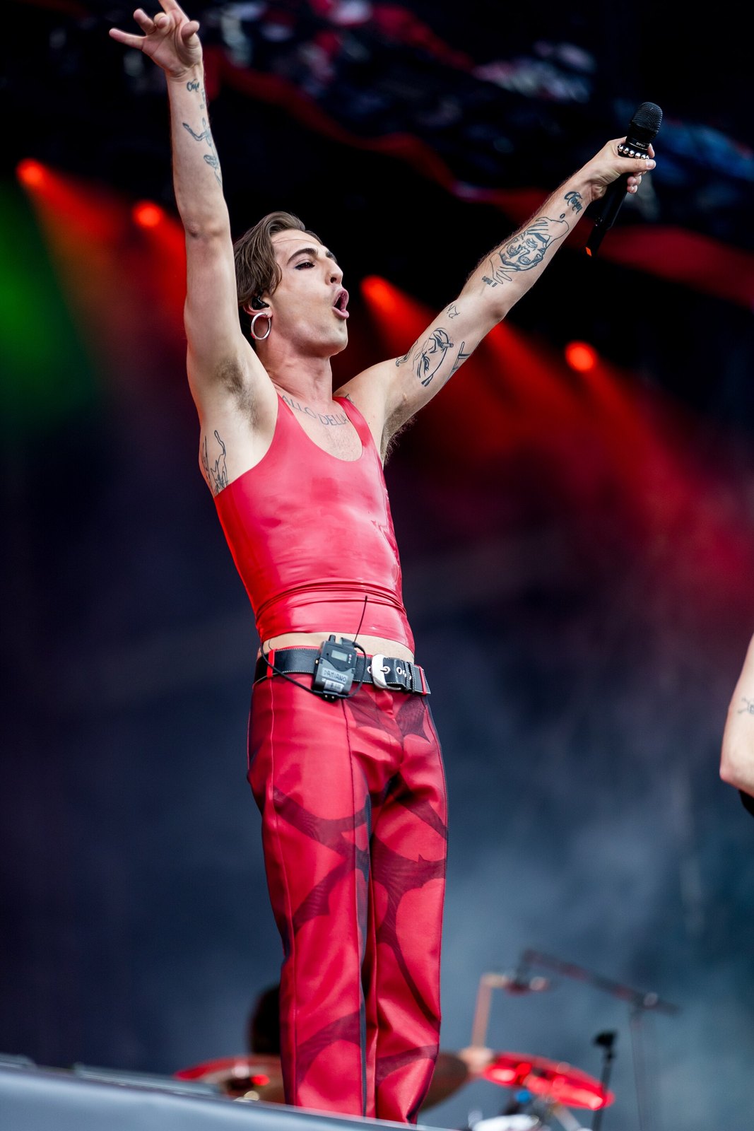 Damiano David dei Måneskin canta sul palco con le braccia alzate, completo rosso