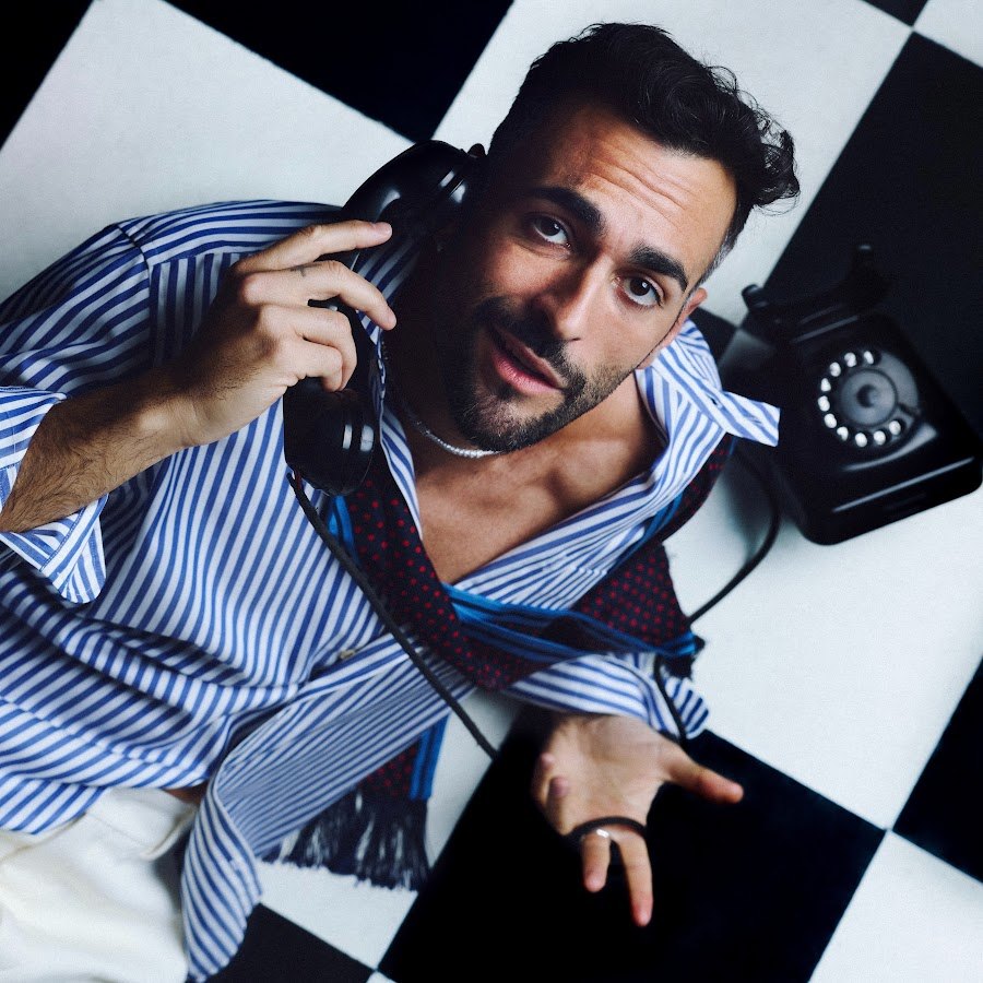 Marco Mengoni guarda verso l'alto con la cornetta di un telefono all'orecchio