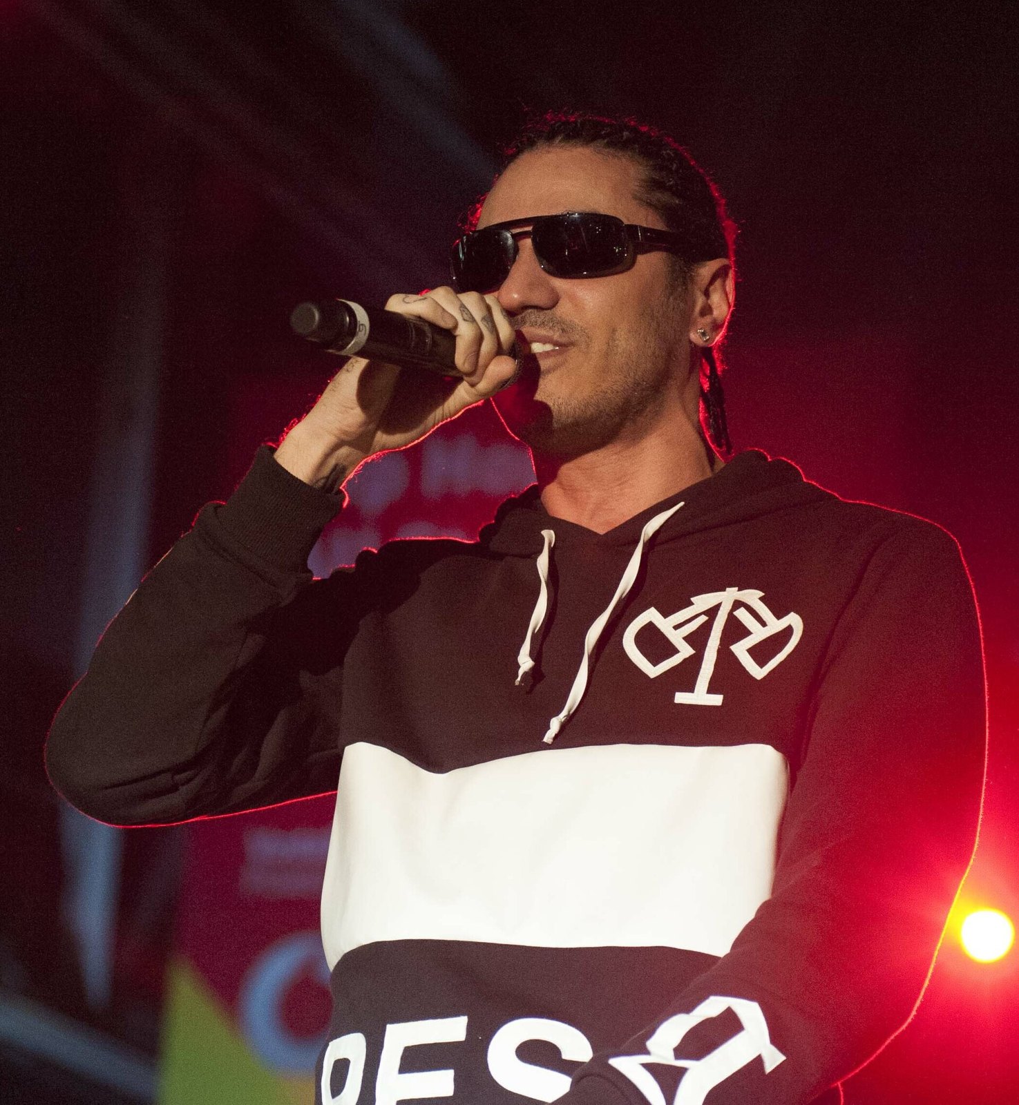 Marracash canta al microfono sul palco, con occhiali da sole scuri