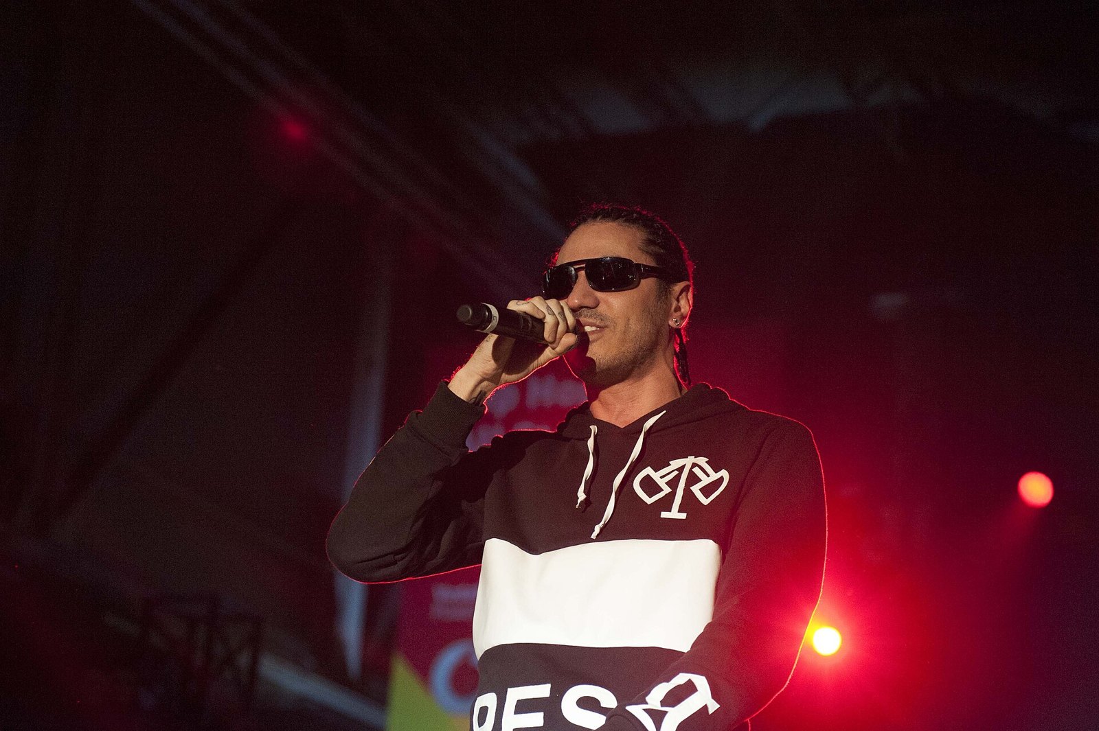 Marracash canta al microfono con gli occhiali da sole, luci rosse alle spalle
