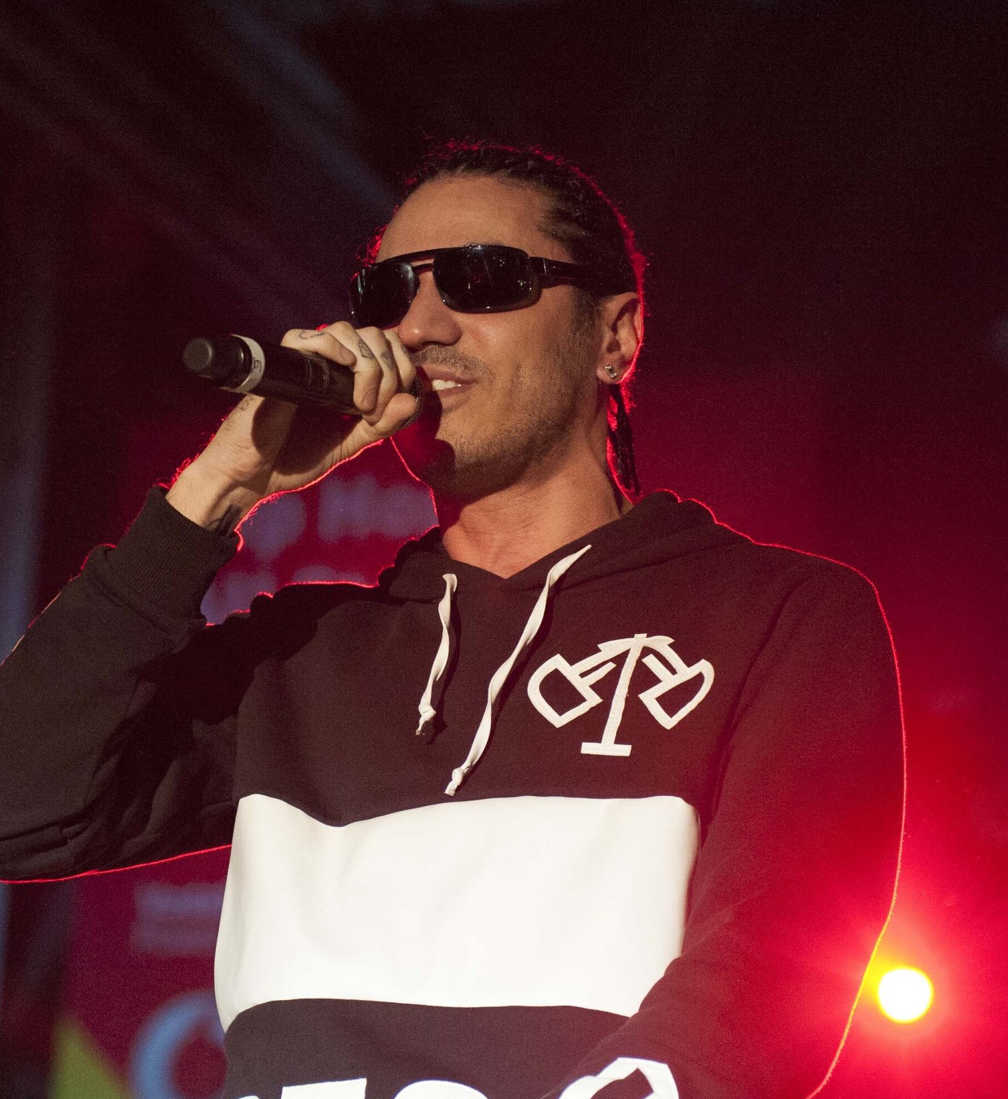 Marracash canta al microfono con occhiali scuri sotto le luci rosse del palco