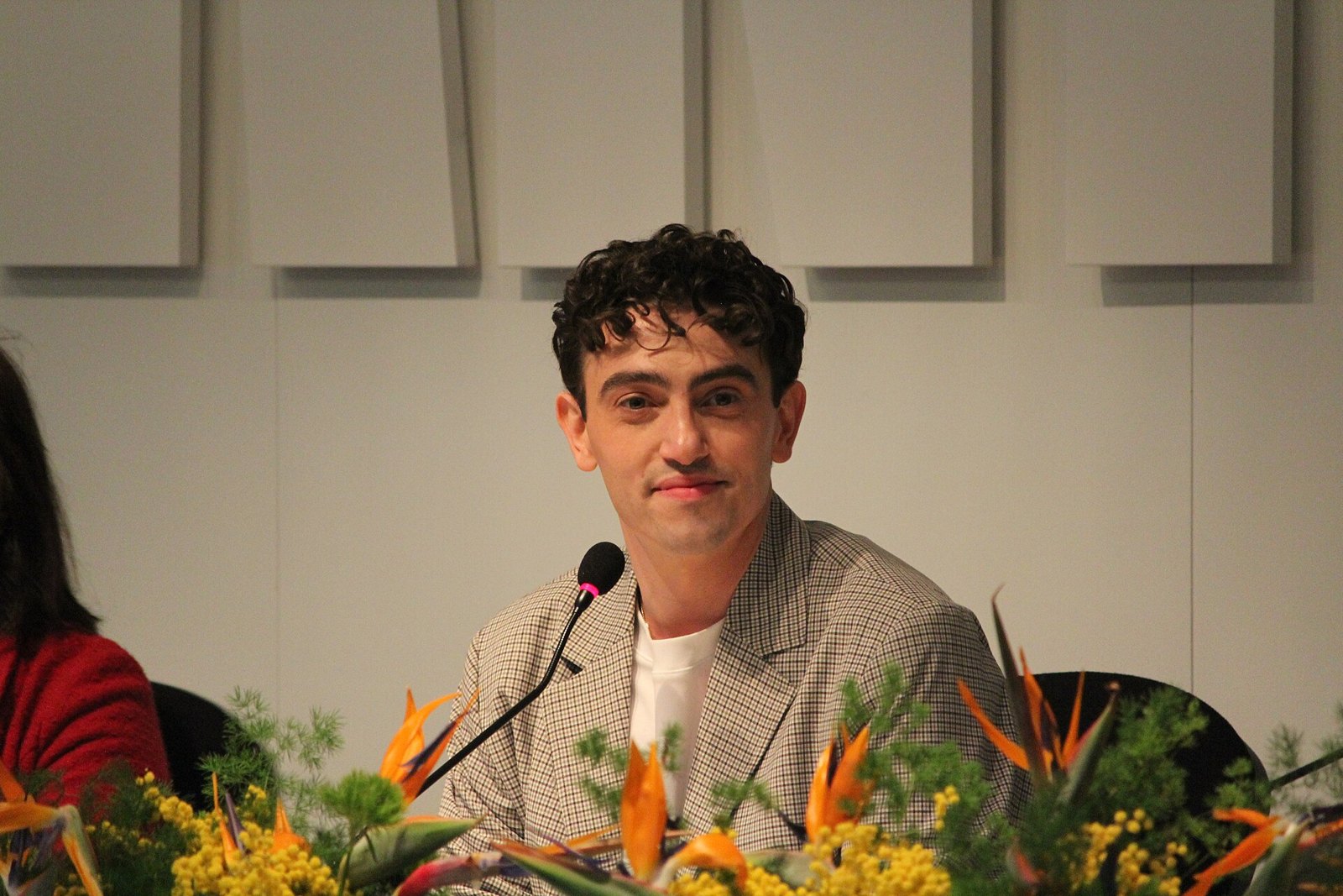 Michele Bravi sorride seduto a un tavolo durante una conferenza stampa