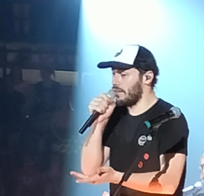 Riccardo Zanotti dei Pinguini Tattici Nucleari canta al microfono con un cappellino bianco e blu