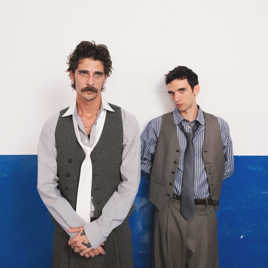 I due Santi Francesi in piedi davanti a un muro bianco e blu, gilet e camicia a righe