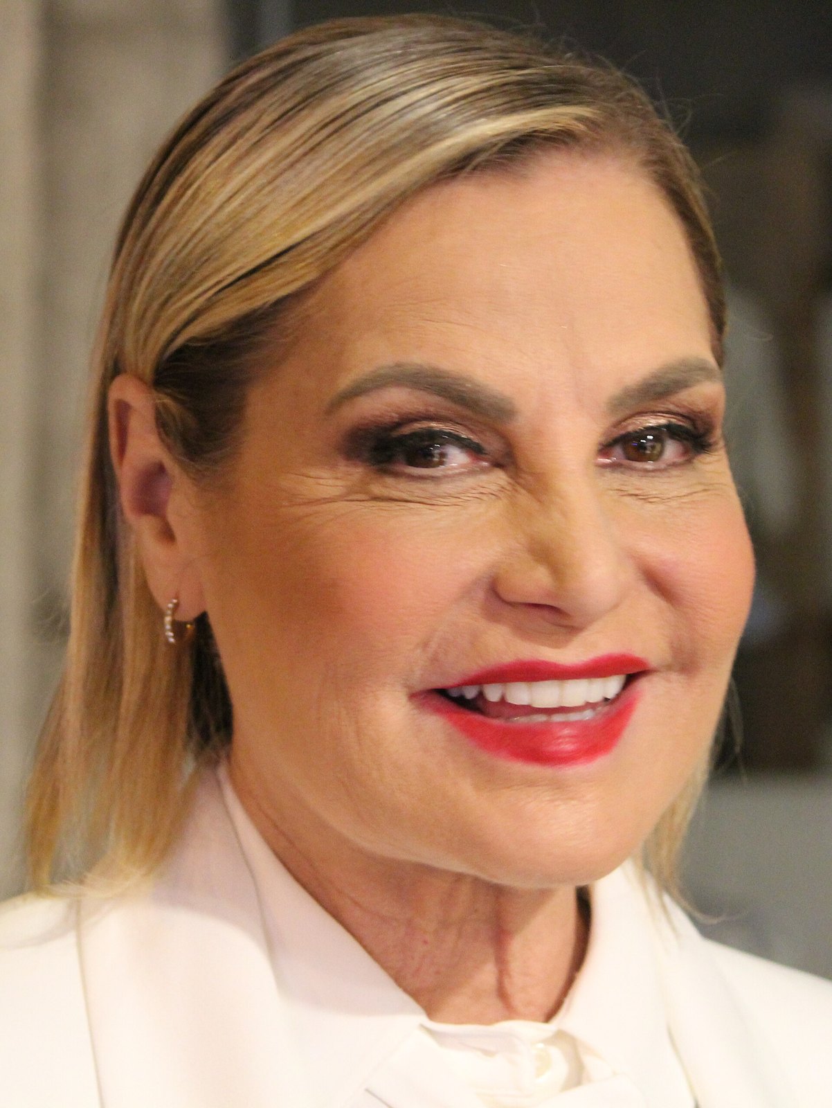 Simona Ventura sorride di profilo con un abito bianco