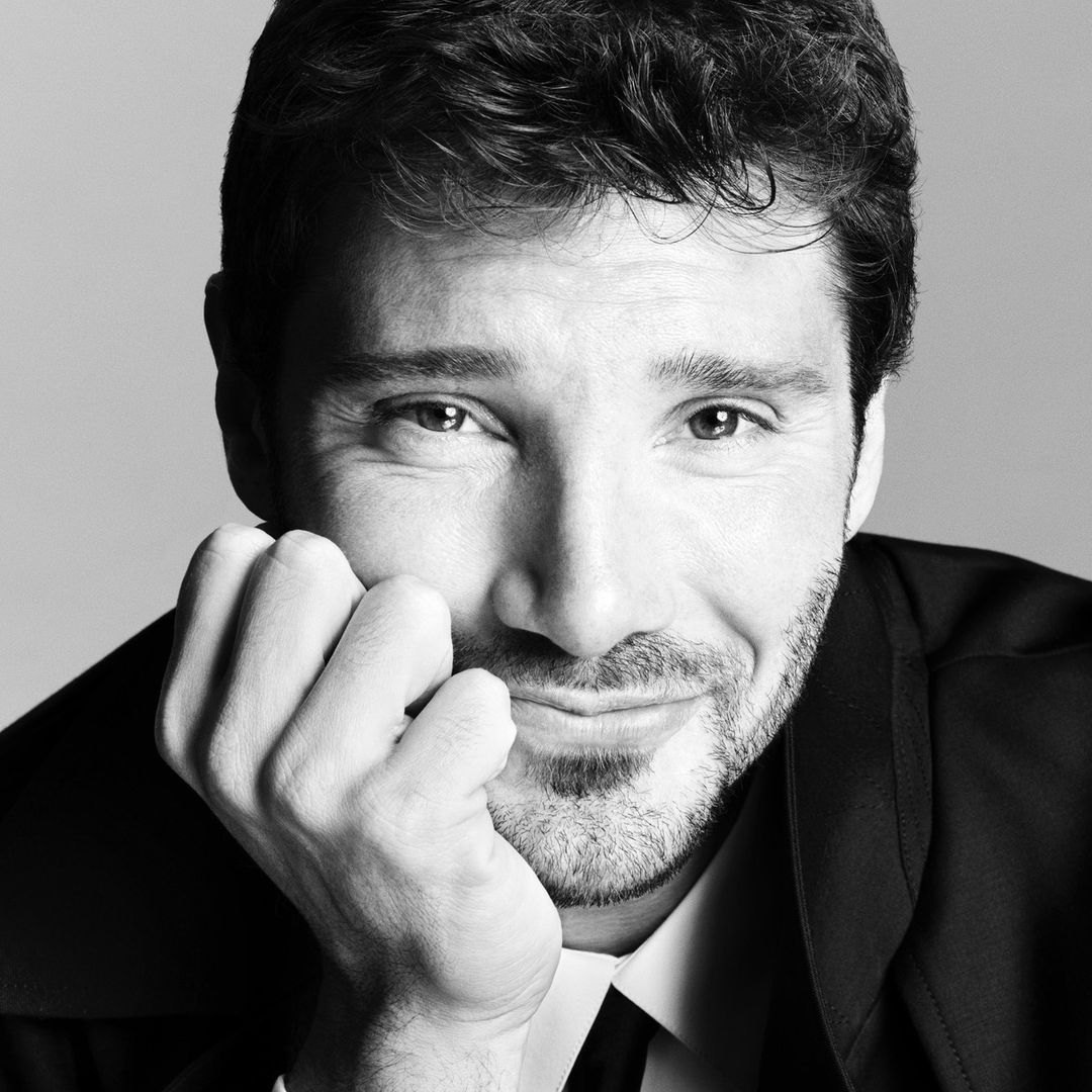 Stefano De Martino sorride in un ritratto in bianco e nero, con il mento appoggiato alla mano