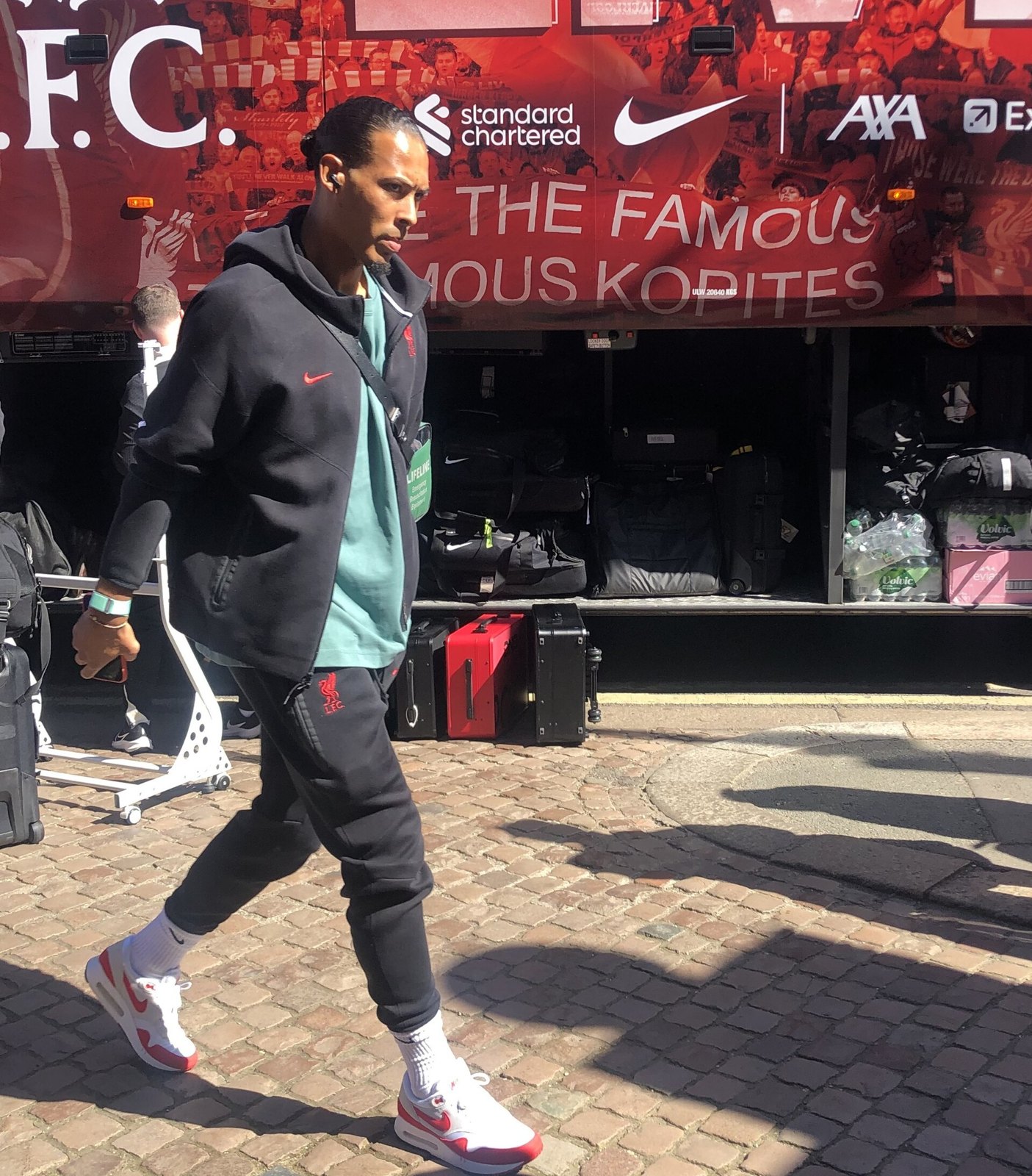 Virgil van Dijk cammina davanti al pullman del Liverpool, in tuta scura e cuffiette